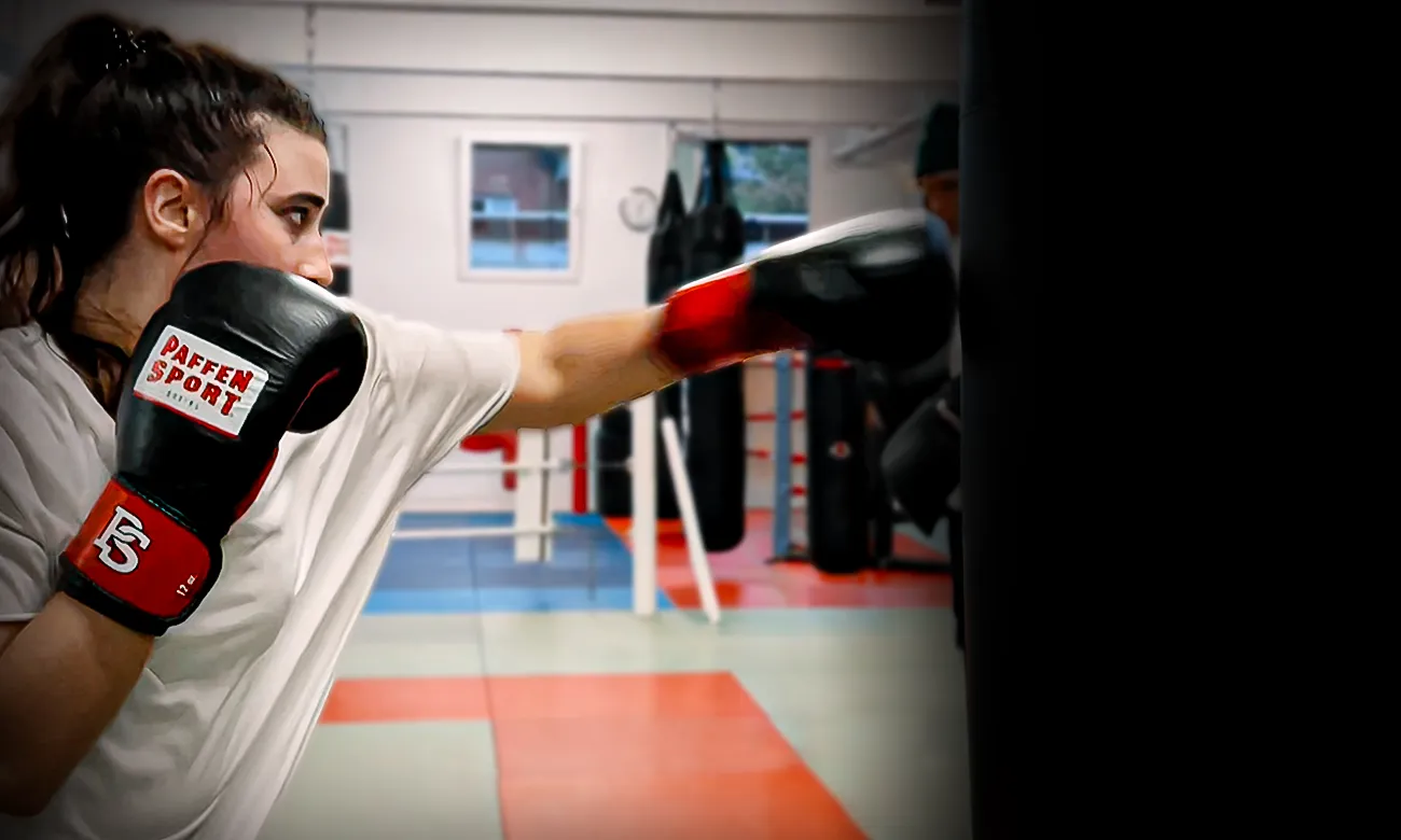 Junge Frau in Boxhandschuhen am Sandsack beim Fitnessboxen in Köln im Combat Club Cologne Gym