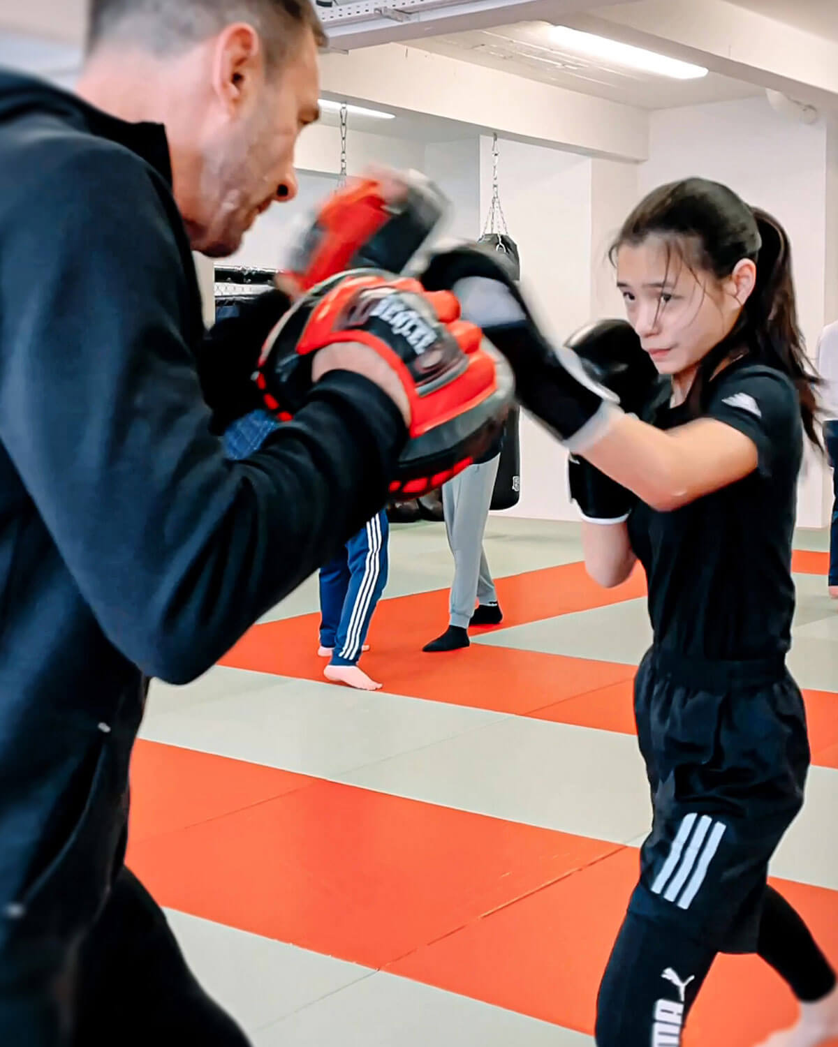 Ein Trainer hält Pratze für ein Mädchen beim Boxen für Kinder in Köln