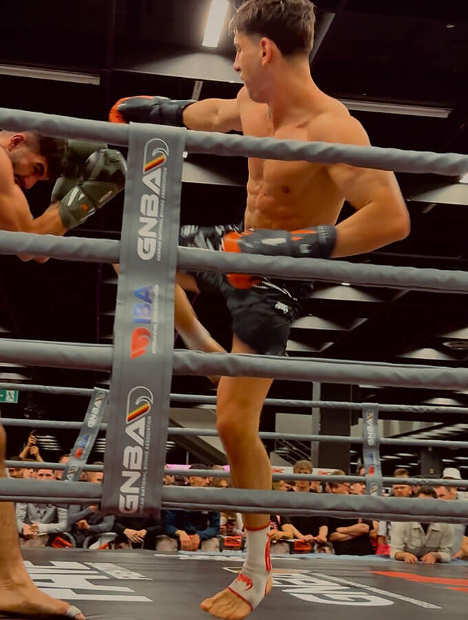 Kickboxen Köln: Ein K1-Sieg auf der FIBO 2025 bei der GMC Olympix Veranstaltung. 2 K1-Kämpfer kämpfen im Boxring gegeneinander. Der Fighter vom Combat Club setzt gerade zu einem wirkungsvollen Kick ein.