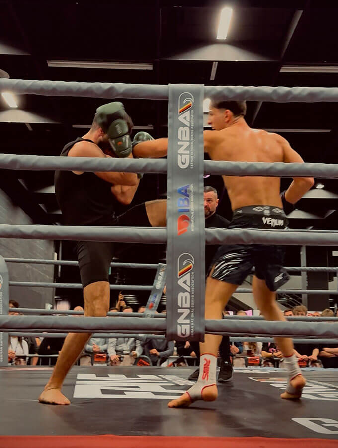 Kickboxen Köln: Ein K1-Sieg auf der FIBO 2025 bei der GMC Olympix Veranstaltung. 2 K1-Kämpfer kämpfen im Boxring gegeneinander. Der Fighter vom Combat Club setzt gerade zu einem wirkungsvollen Schlag ein.