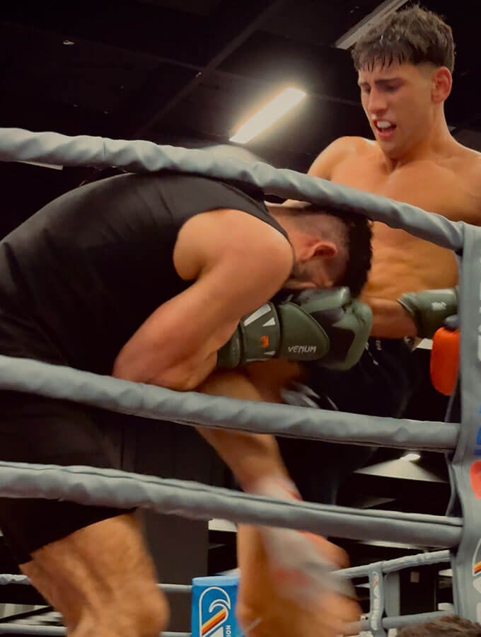 Kickboxen Köln: Ein K1-Sieg auf der FIBO 2025 bei der GMC Olympix Veranstaltung. 2 K1-Kämpfer kämpfen im Boxring gegeneinander. Der Fighter vom Combat Club setzt gerade zu einem wirkungsvollen Knie zum Körper ein.